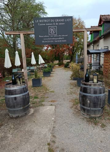 Allée bordée de tonneaux sous le panneau du Bistrot du Grand Liot