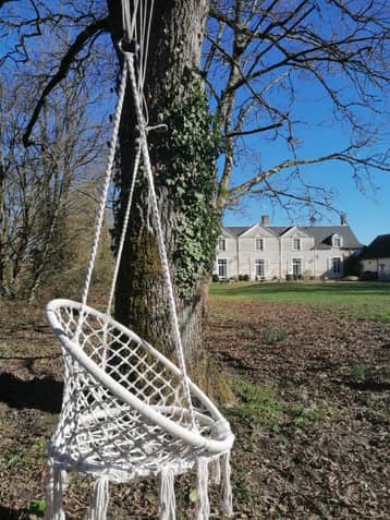 Fauteuil suspendu en macramé, accroché à un arbre, le manoir au fond