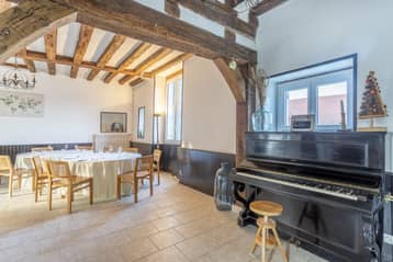 Salon du manoir avec piano et grandes tables, sous les poutres