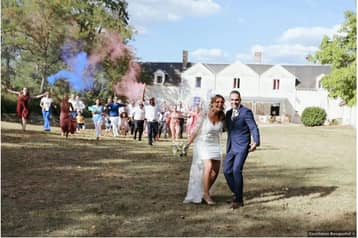 Mariés qui marchent sur la pelouse devant le manoir, fumigènes colorés