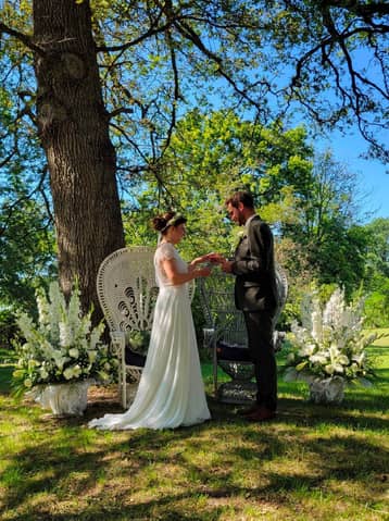 Mariés face à face sous un arbre, fleurs blanches autour d'eux