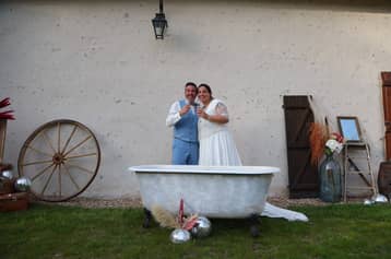 Mariés dans une baignoire ancienne sur la pelouse, roue de charrette derrière eux