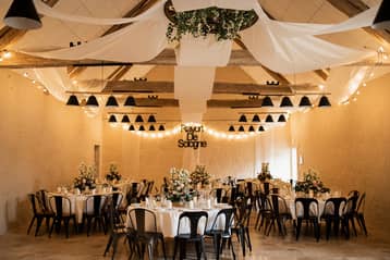 Grange éclairée en soirée, voilages et tables rondes