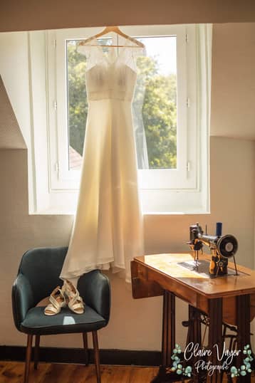 Robe de mariée suspendue à la fenêtre, machine à coudre ancienne au premier plan