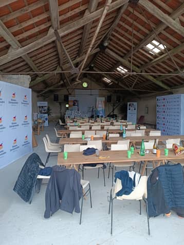 Grange aménagée pour un séminaire, longues tables et banderoles devant la scène