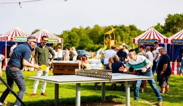 Partie de ping-pong en extérieur lors d'une soirée, tentes rayées au fond