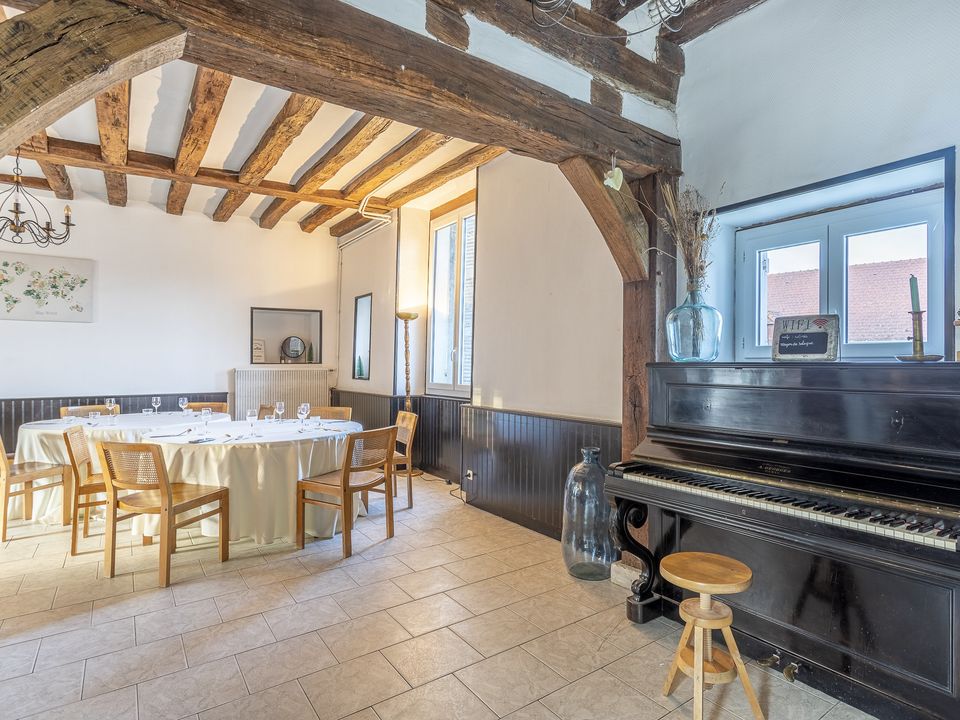 Salon du manoir avec piano et grandes tables, sous les poutres