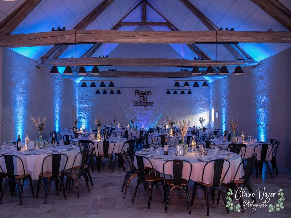 Grange illuminée en bleu, tables rondes dressées pour une réception