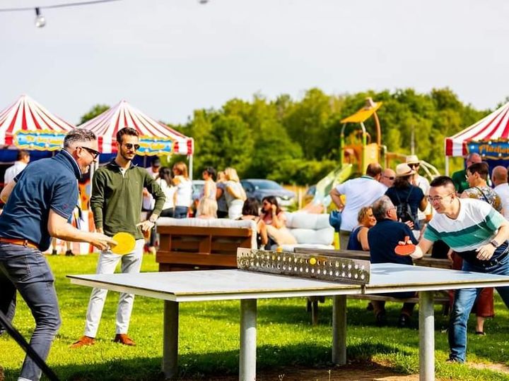 Partie de ping-pong en extérieur lors d'une soirée, tentes rayées au fond