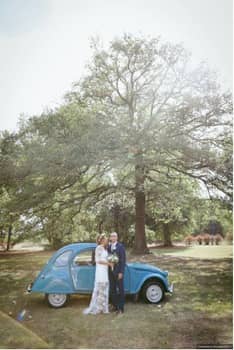 Mariés devant une voiture ancienne bleue, au pied d'un chêne
